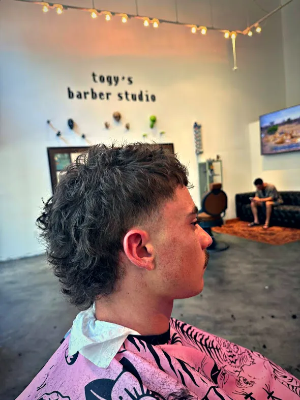Modern mullet with a taper, in front of the pixel-letter wall sign