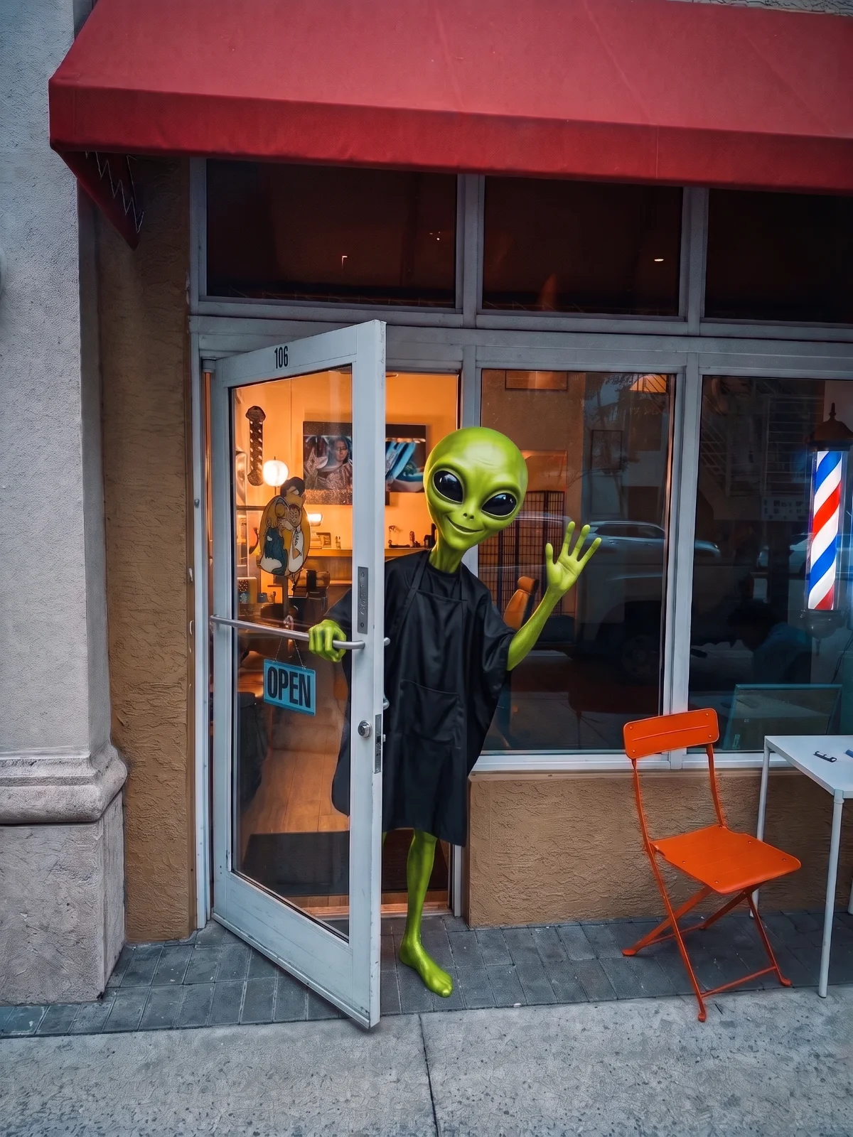 The front door of Togy's Barber Studio, unit 106, under a red awning, with an alien holding the door open and waving visitors in